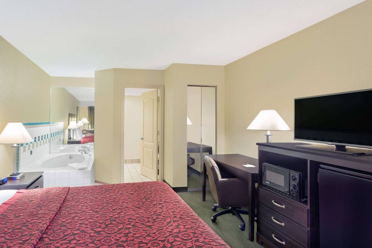 Una camera d'albergo con un letto, una scrivania, televisione e bagno visibile attraverso una porta aperta.