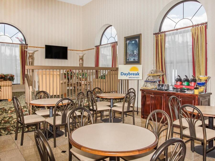 A hotel breakfast area with round tables and chairs, a Daybreak breakfast sign, and a buffet counter.