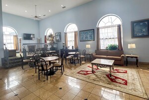 Un comedor amplio con varias mesas y sillas, ventanas grandes con cortinas y suelo de baldosas.