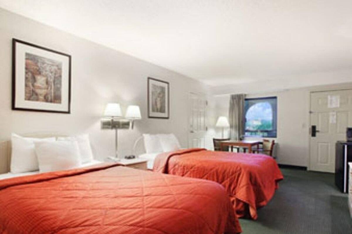 Una camera d'albergo con due letti, una scrivania, una sedia, una televisione e una finestra con vista.