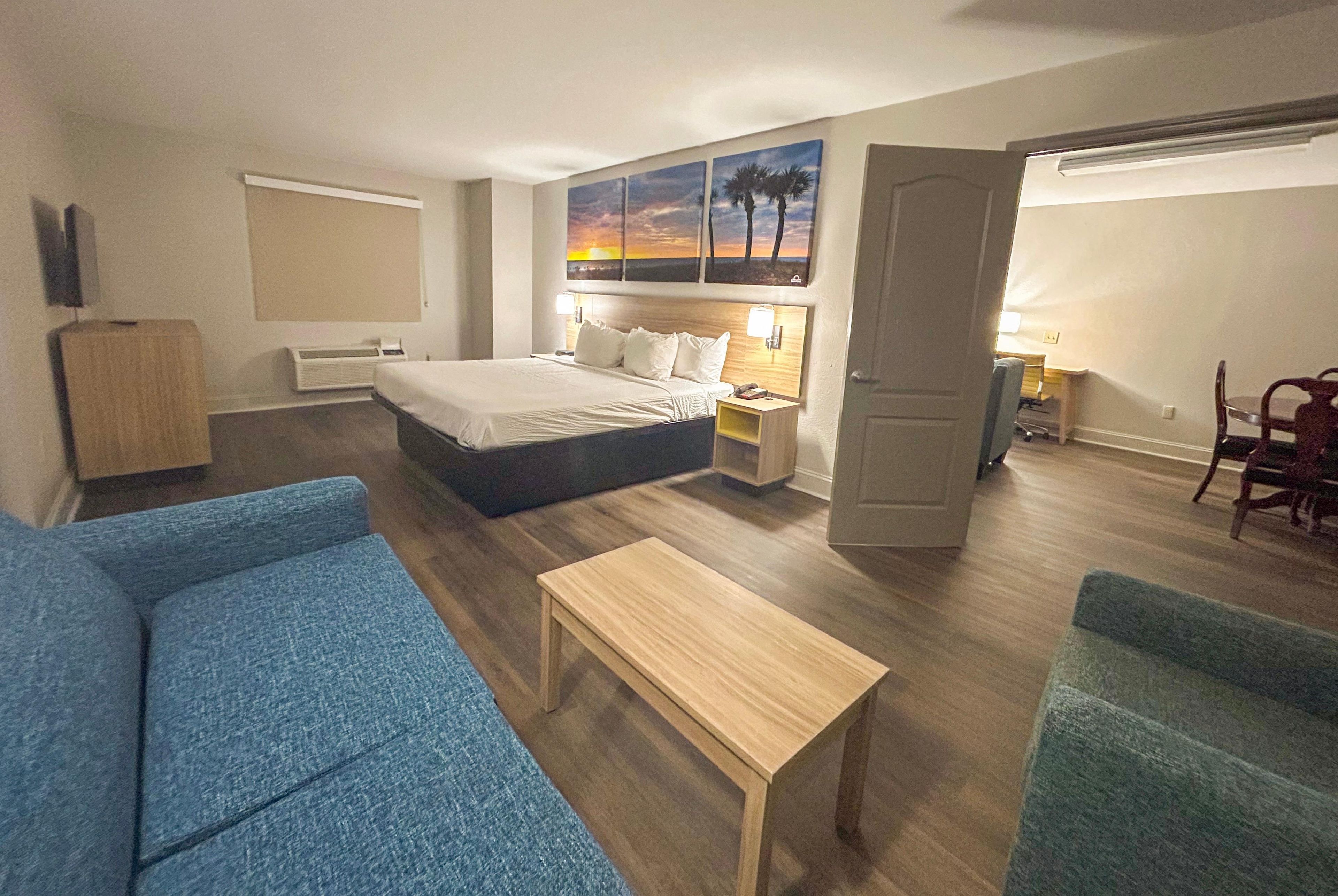 A hotel room with a bed, a desk, a chair, a sofa, and a painting on the wall.