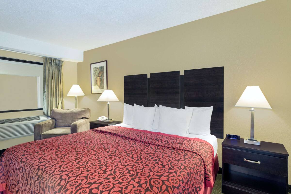 Camera d'albergo con un letto grande, due comodini con lampade, una sedia e una finestra con tende.