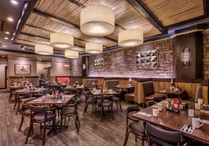 Un restaurante con varias mesas y cabinas, piso de madera y una pared de piedra con diseños geométricos.