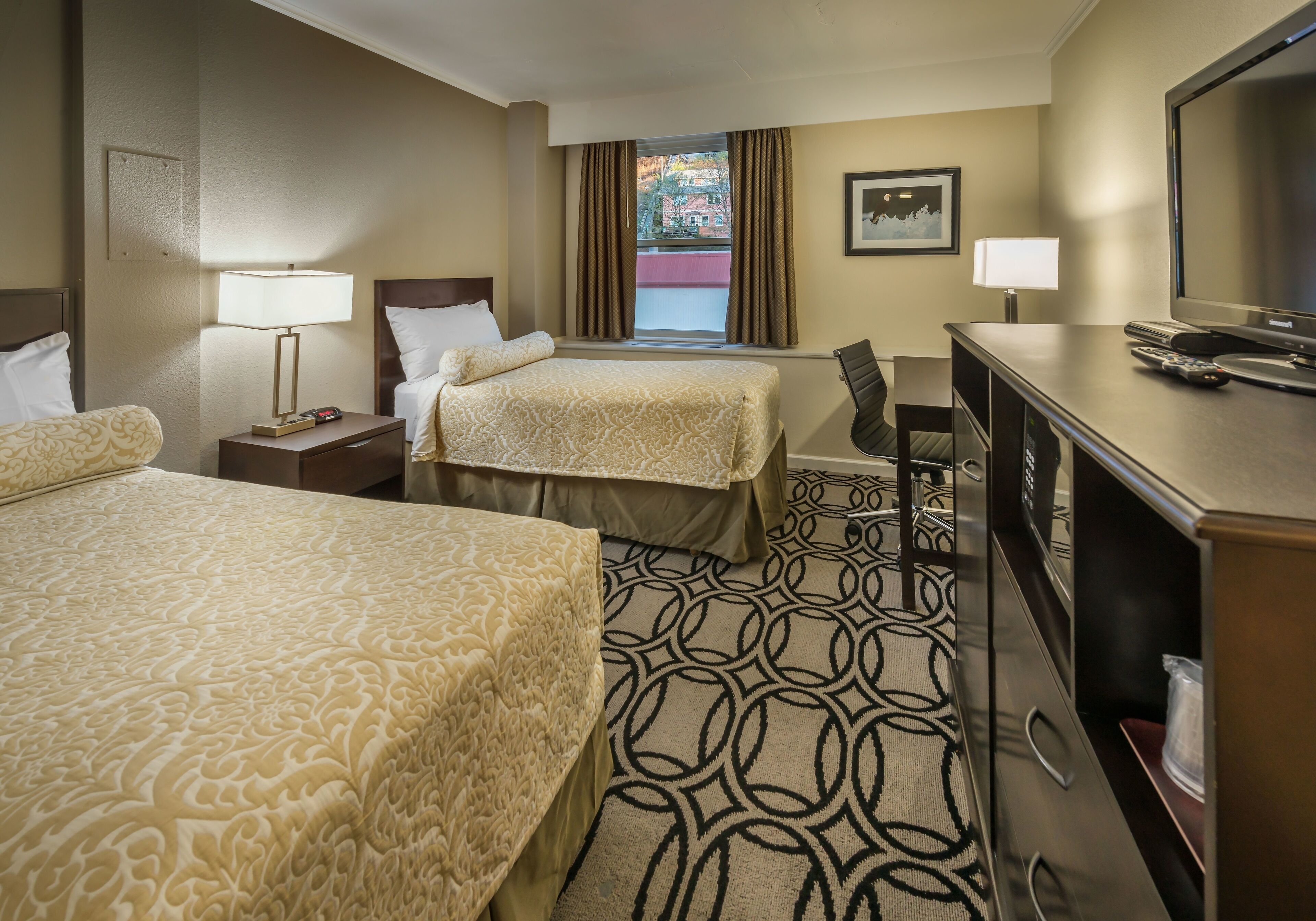 A hotel room with two beds, a desk, a television, and a window with curtains.