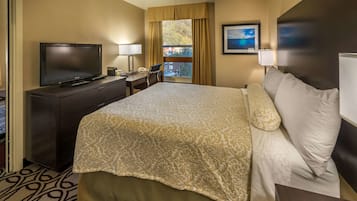 A hotel room with a large bed, a TV, a desk with a chair, and a window with curtains.