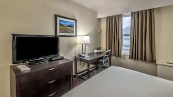 Hotelkamer met een bed, een bureau met stoel, een televisie, een lamp, een ingelijst schilderij aan de muur en een raam met gordijnen.