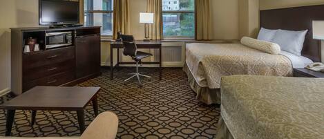 A hotel room with two beds, a desk with a chair, a television, a microwave, and a coffee maker.