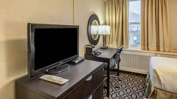 Une chambre d’hôtel équipée d’un téléviseur à écran plat, d’un bureau avec une lampe, d’une chaise, d’un lit et d’une fenêtre avec des rideaux.