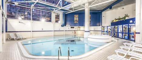 An indoor swimming pool with clear blue water, surrounded by white lounge chairs and a high ceiling with skylights.