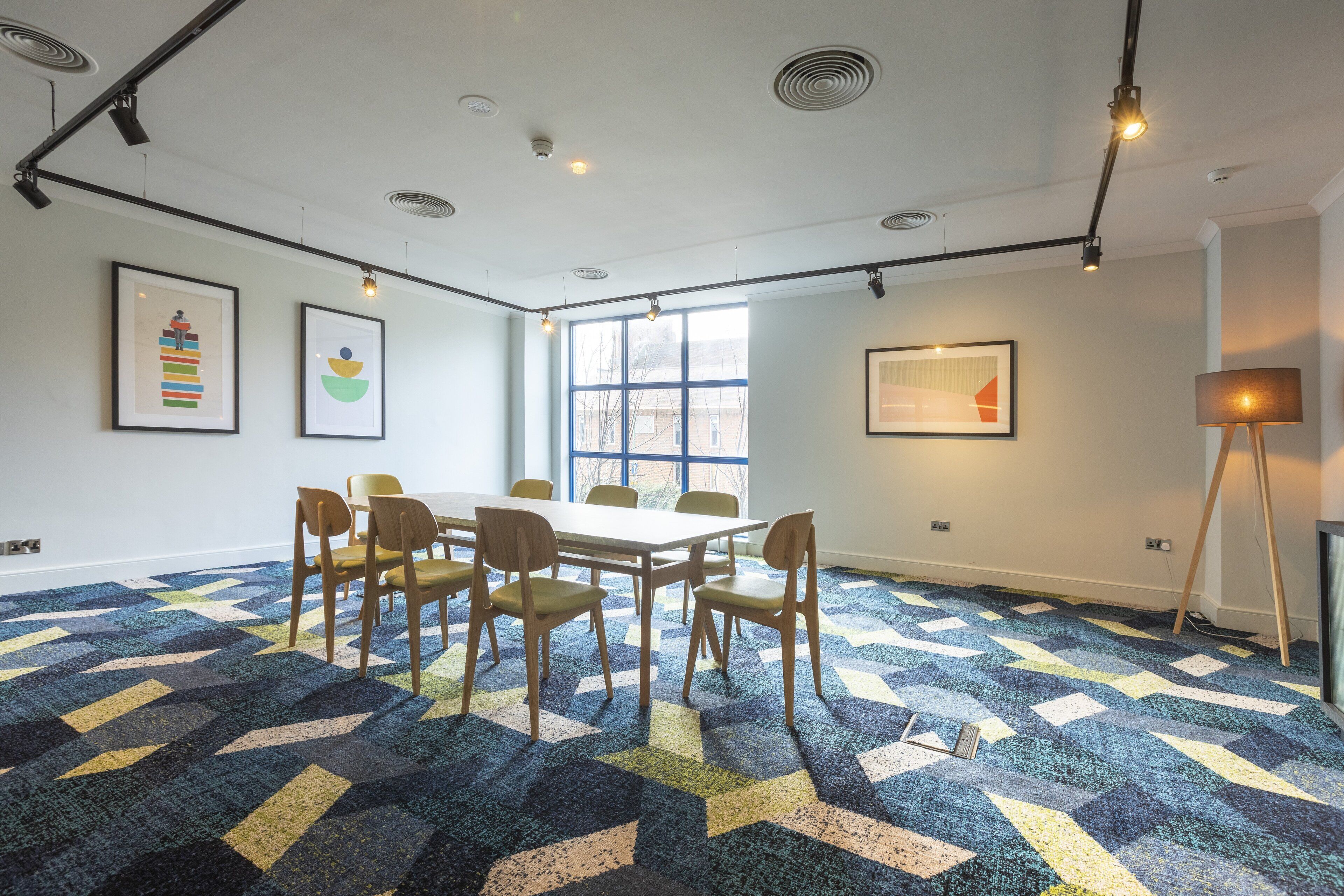 A conference room with a large table, six chairs, and a patterned carpet.