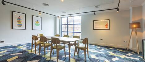 A conference room with a large table, six chairs, and a patterned carpet.