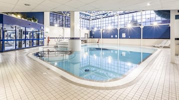 An indoor swimming pool with clear water, surrounded by tiled flooring and walls.