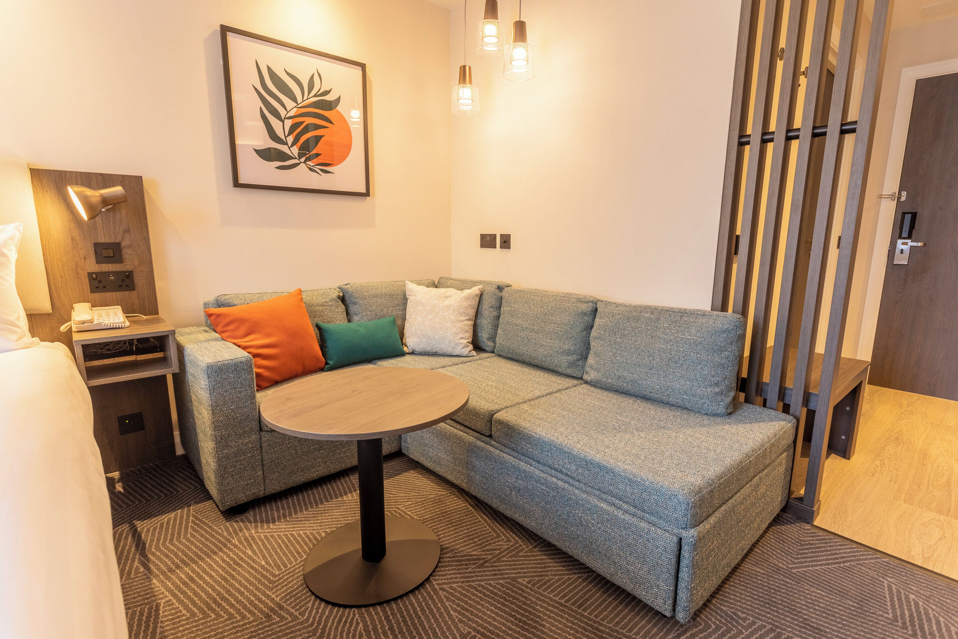 A modern living room with a sectional sofa, a round coffee table, a wall-mounted lamp, and a framed artwork.