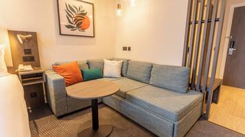 A modern living room with a sectional sofa, a round coffee table, a wall-mounted lamp, and a framed artwork.