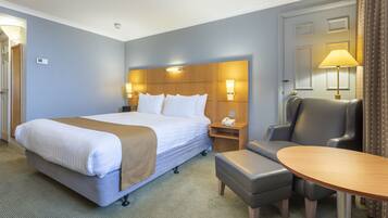 Une chambre d’hôtel avec un grand lit, un bureau avec une chaise, une lampe et une porte avec des rideaux.
