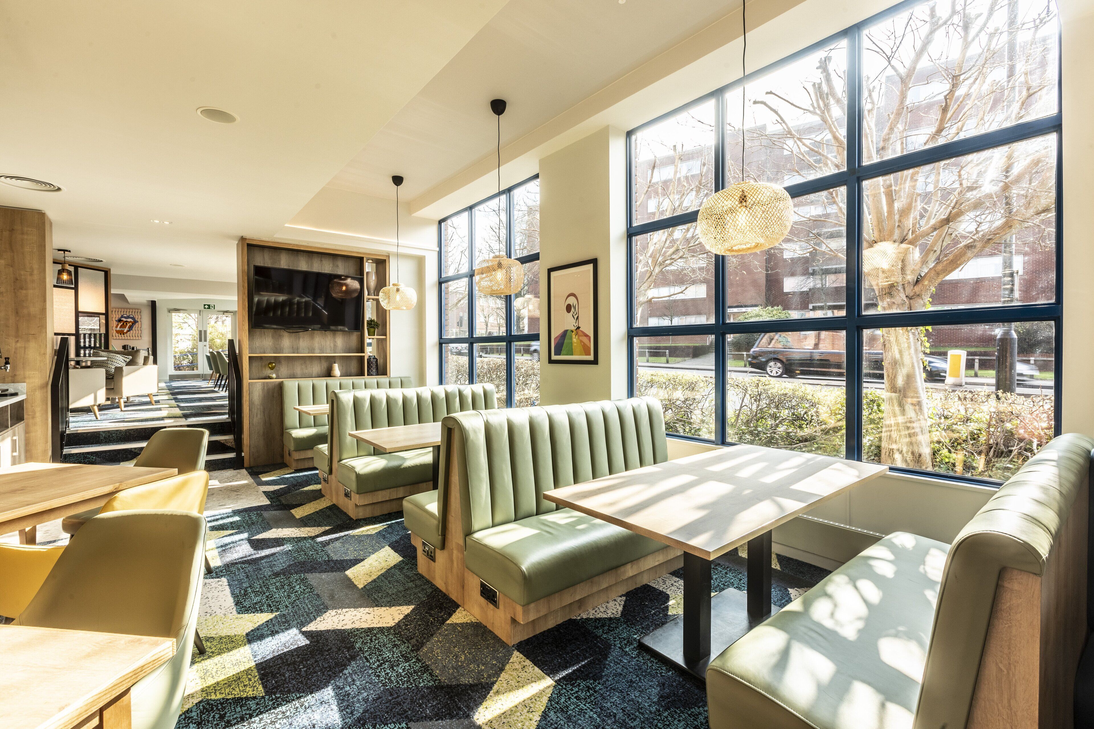 Een modern restaurant met groene banken en een patroon vloer, grote ramen met uitzicht en hanglampen.