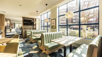Een modern restaurant met groene banken en een patroon vloer, grote ramen met uitzicht en hanglampen.