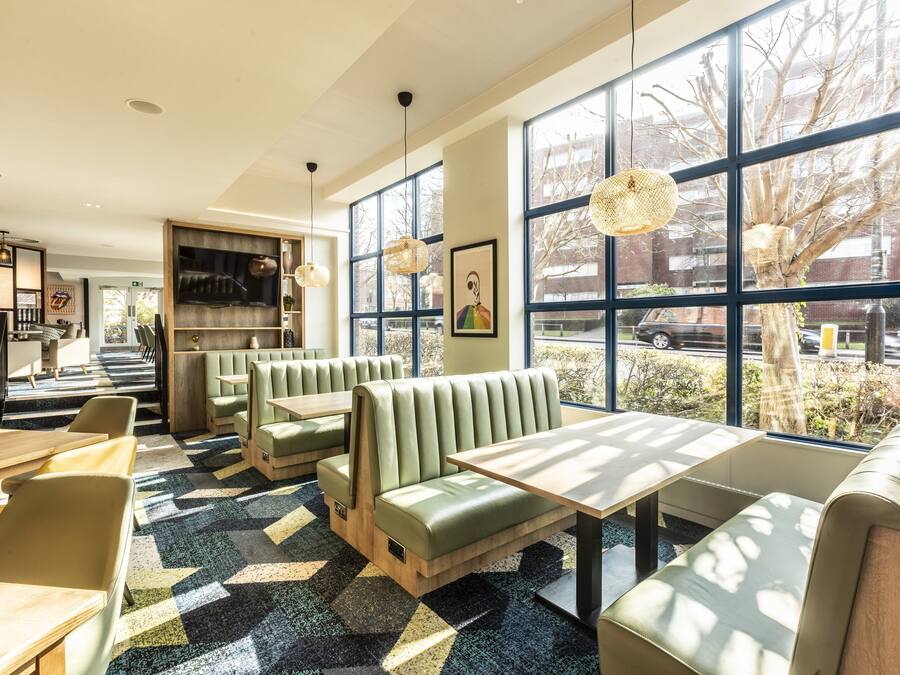 Een modern restaurant met groene banken en een patroon vloer, grote ramen met uitzicht en hanglampen.