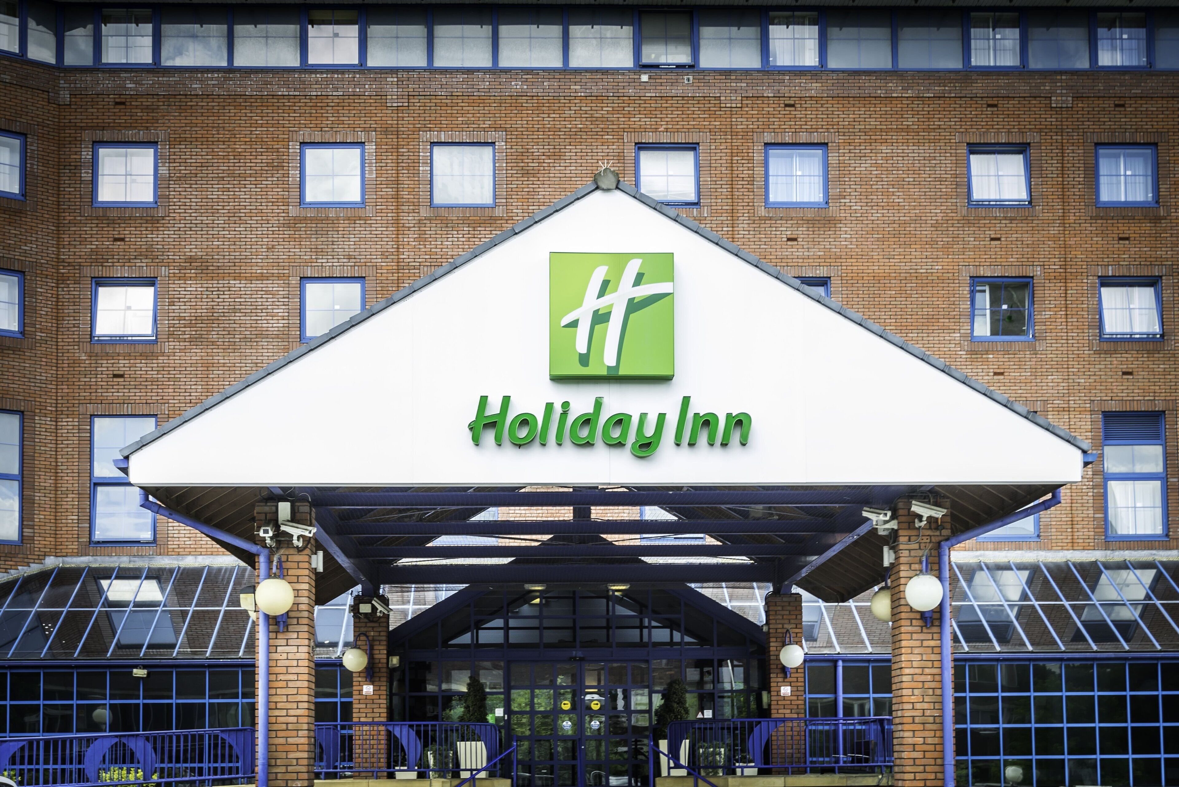 A Holiday Inn hotel entrance with a brick facade, large windows, and a covered entrance area.