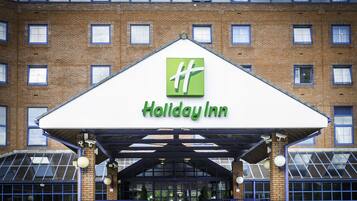 Entrada de un hotel Holiday Inn, con fachada de ladrillo, ventanas grandes y zona de acceso cubierta.