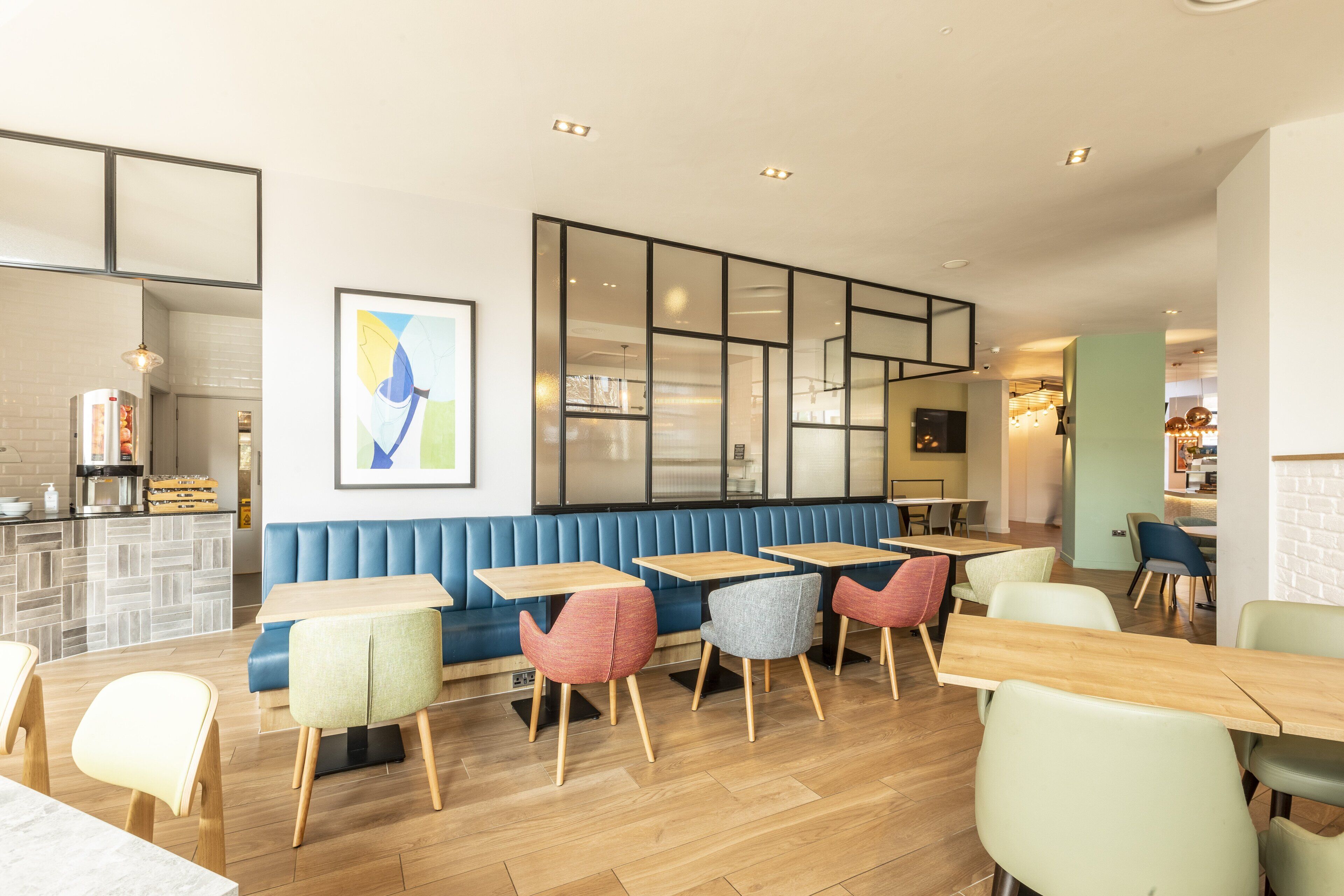 A modern restaurant interior with wooden tables and chairs, a blue booth seating area, and a large abstract painting on the wall.