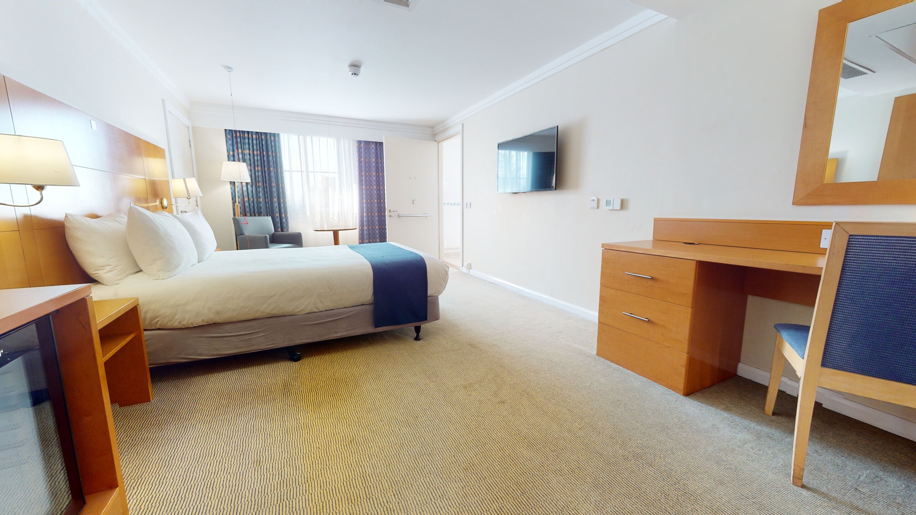 A hotel room with a bed, desk, chair, and a television on the wall.