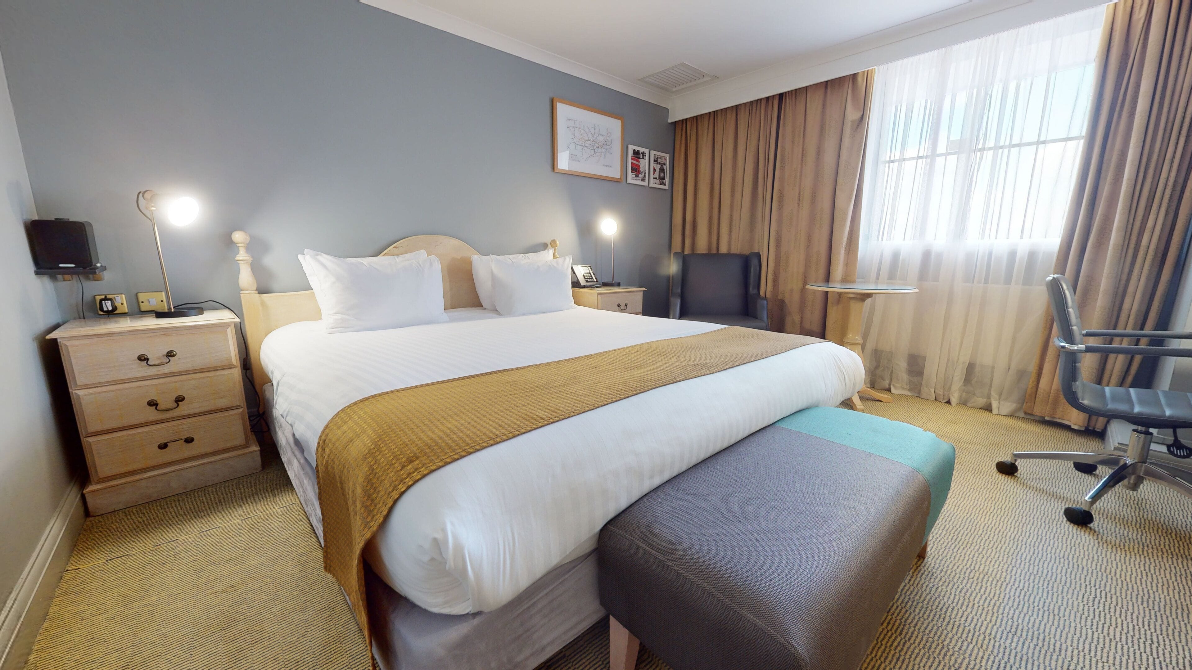 Ein Hotelzimmer mit einem großen Bett, Nachttischen, einem Schreibtisch, einem Sessel und einem Fernseher.