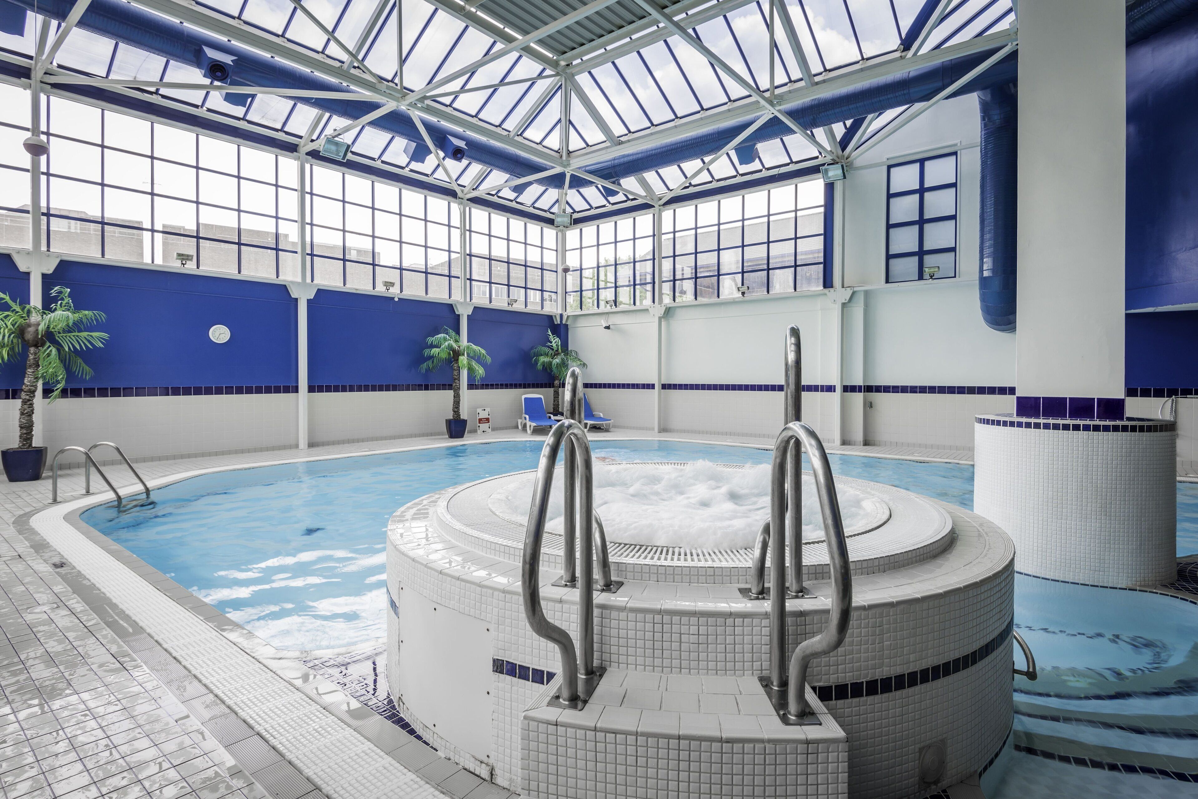 An indoor swimming pool with a glass ceiling, blue walls, and a tiled floor.