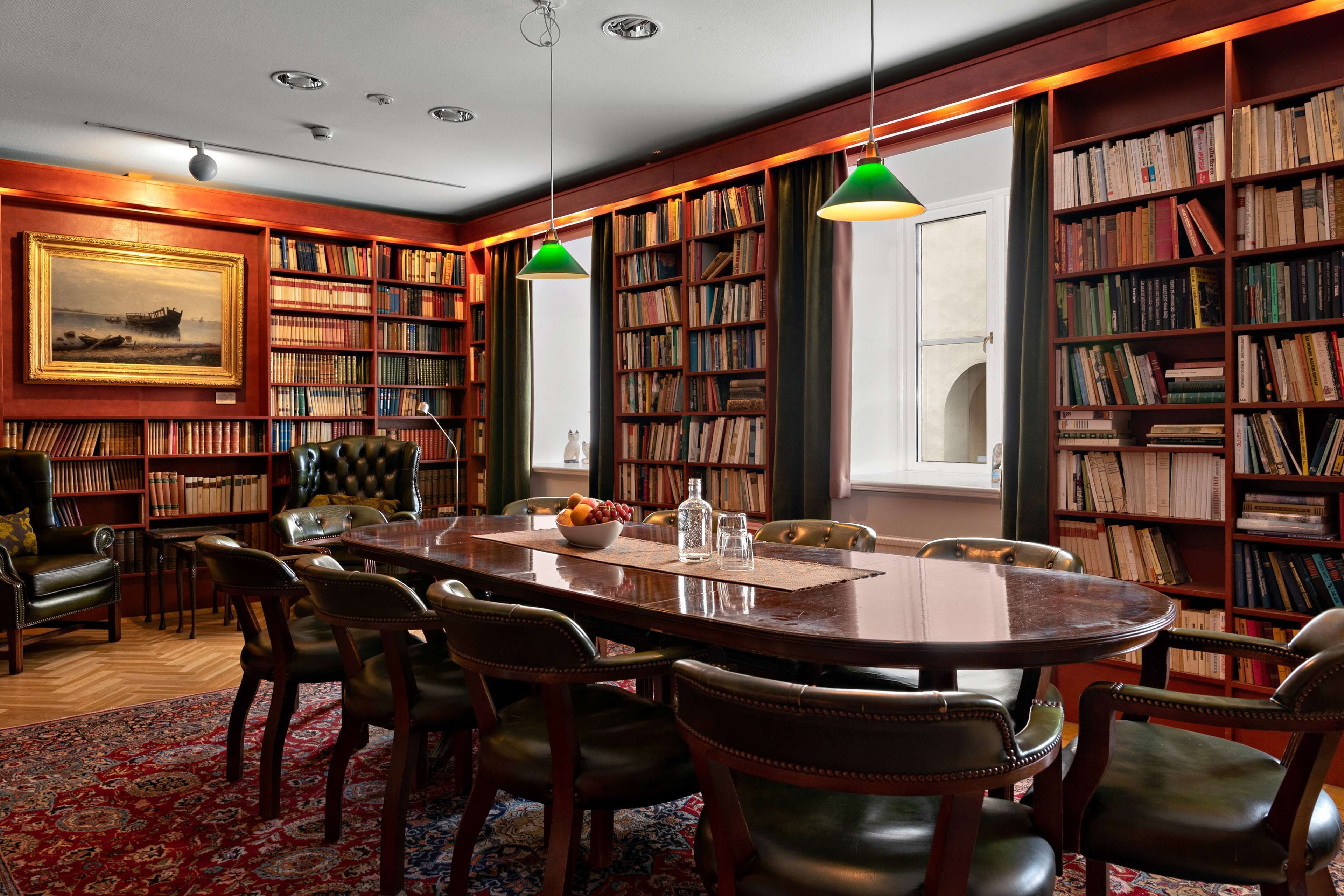 Et bibliotek med et stort træbord, læderstole og reoler fyldt med bøger.