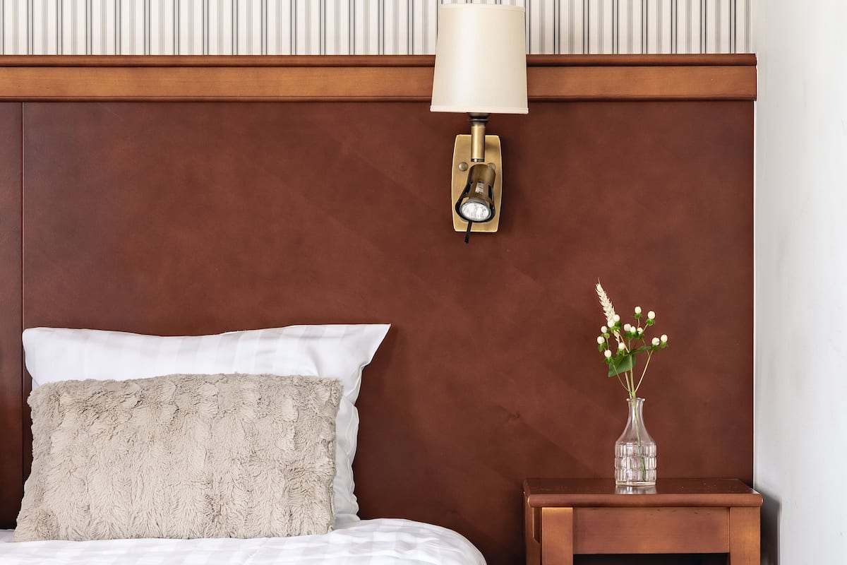 Un lit bien fait, avec un oreiller moelleux, une table de chevet ornée d’un vase de fleurs et une lampe fixée au mur.