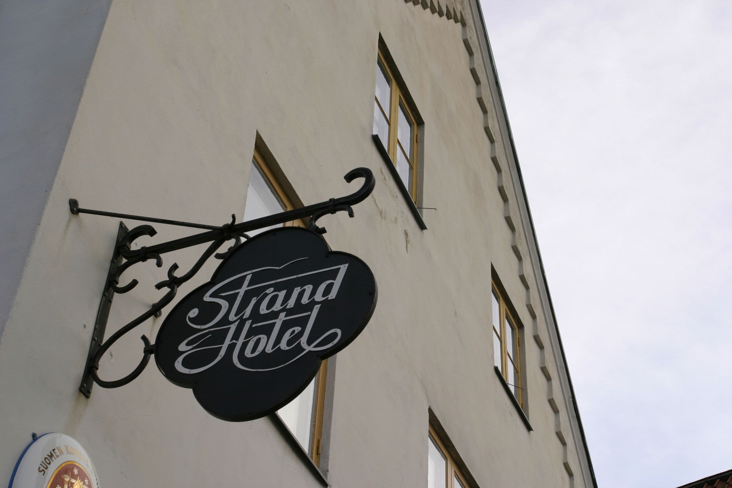 A hotel sign with the name "Grand Hotel" in a classic font, attached to a building with a white facade and multiple windows.