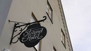A hotel sign with the name "Grand Hotel" in a classic font, attached to a building with a white facade and multiple windows.