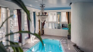 Une piscine intérieure agrémentée d’un lustre, de grandes fenêtres et d’une plante en pot.