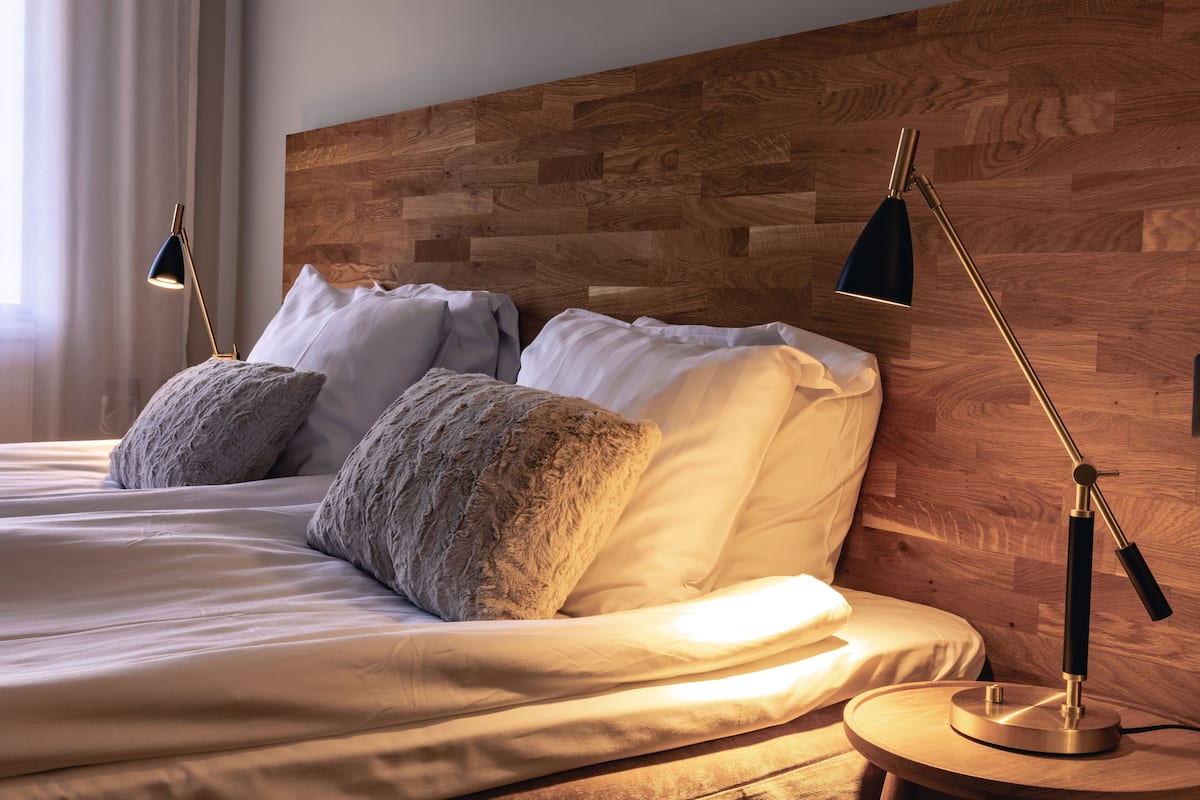 Un lit bien fait, avec du linge de lit blanc et deux coussins décoratifs, une tête de lit en bois et deux lampes de chevet.