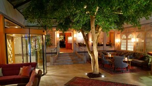 Un hall d’entrée intérieur avec un arbre central, des espaces de détente et un escalier menant à un niveau supérieur.