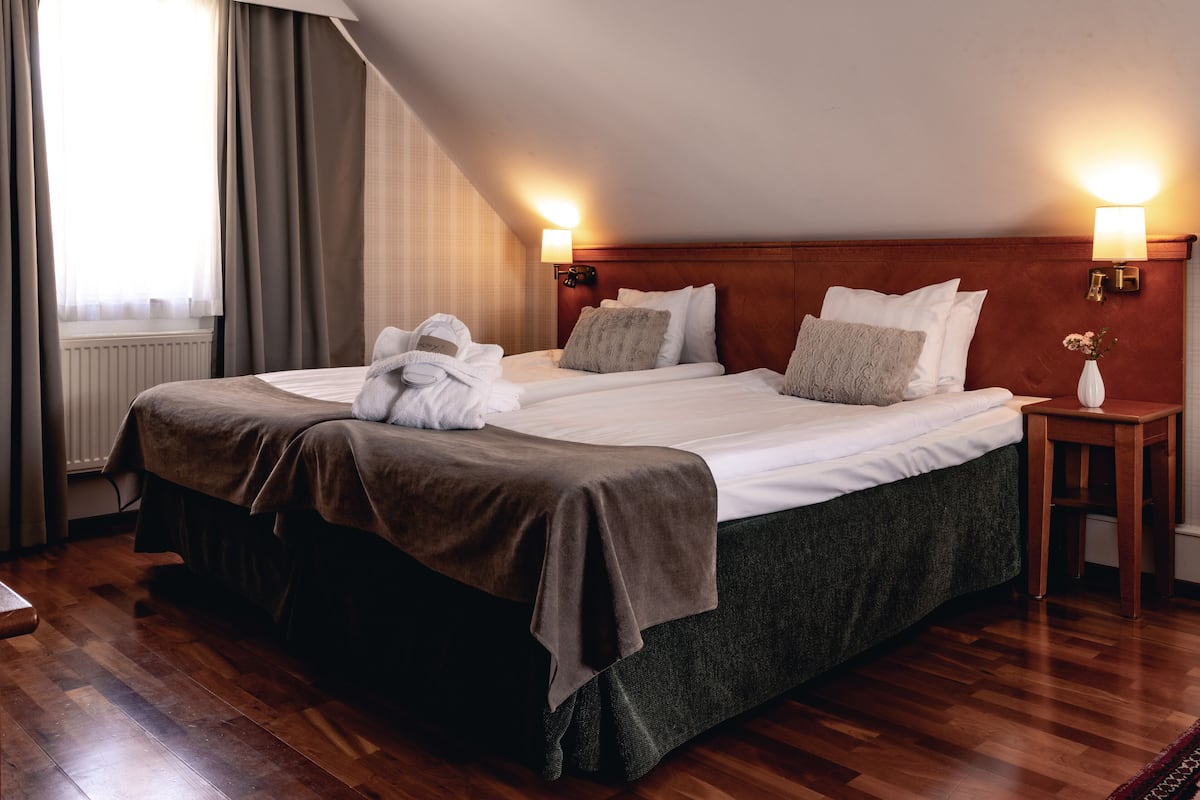Une chambre d’hôtel avec un grand lit, deux tables de chevet, une fenêtre avec des rideaux et un radiateur.