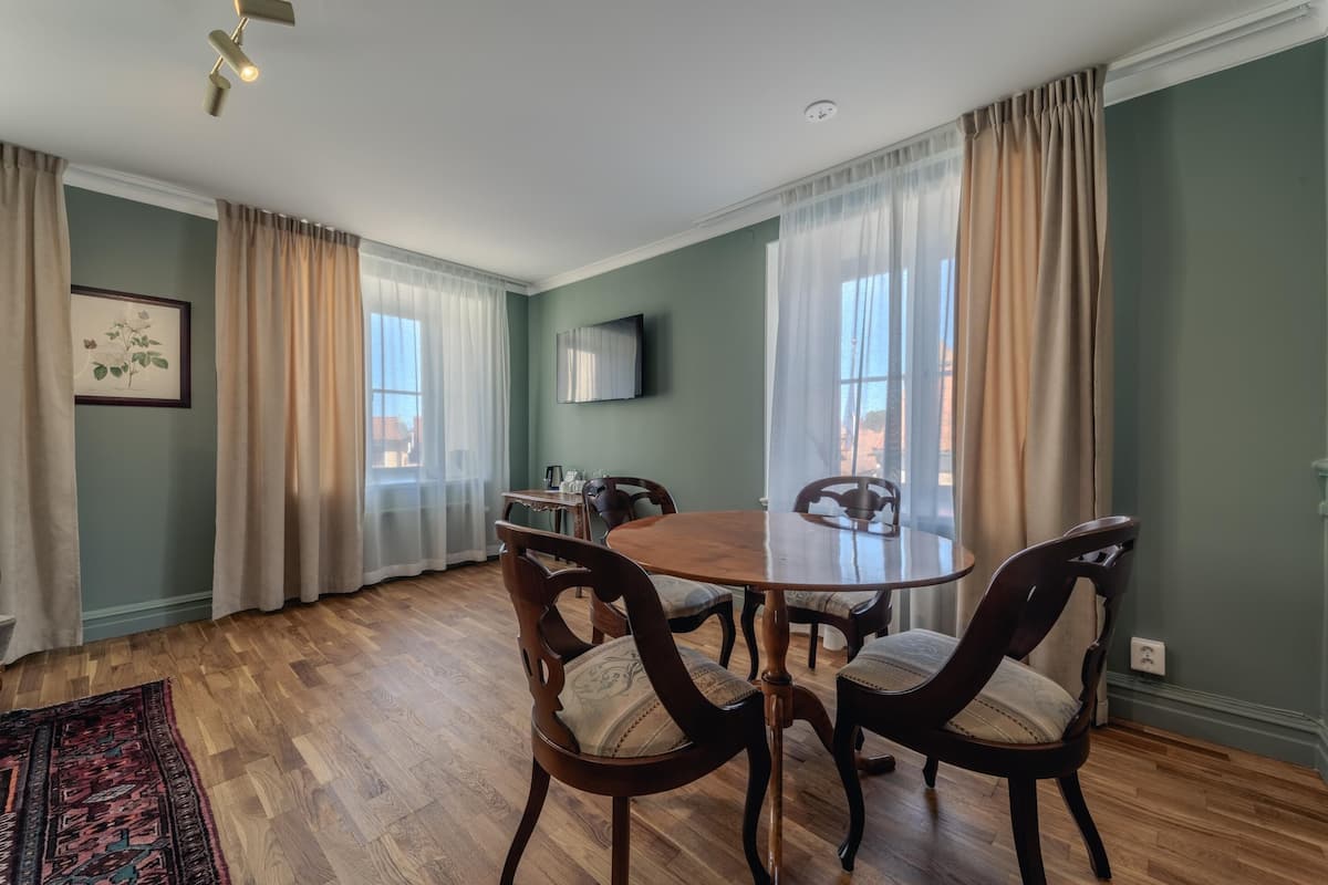 Un coin repas avec une table ronde et quatre chaises, un plancher en bois et des rideaux de couleur claire.