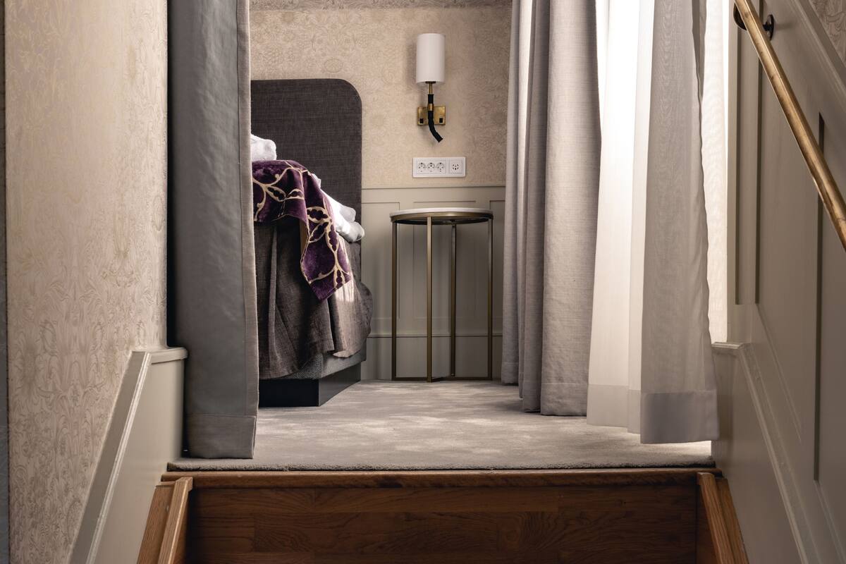 Un escalier menant à une chambre à coucher équipée d’un lit, d’une table de chevet et d’une lampe fixée au mur.