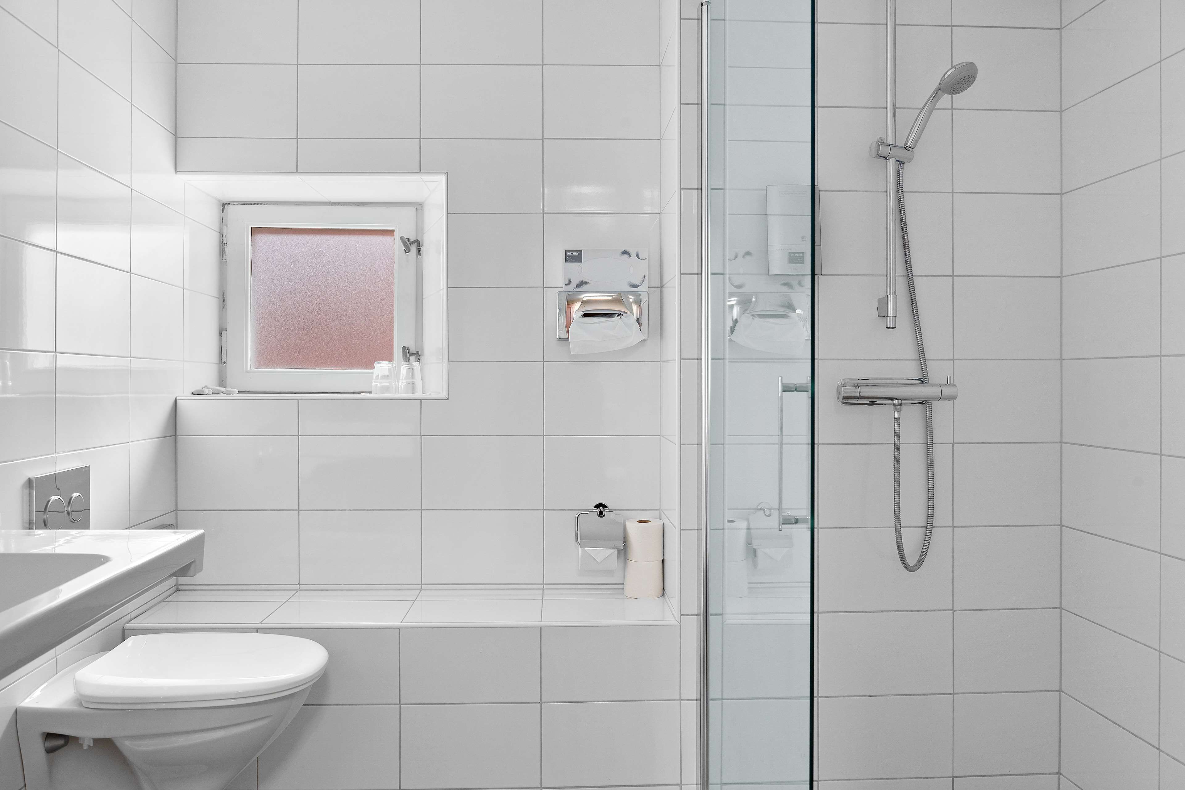 A modern bathroom with a toilet, a glass shower enclosure, and a window.