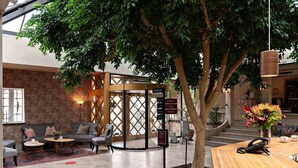 Un hall d’entrée avec un espace salon aménagé en cercle, un comptoir d’accueil et un grand arbre.