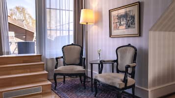 Una habitación con dos sillones tapizados, una mesita con un jarrón, una lámpara de pie y una escalera que conduce a un espacio al aire libre.