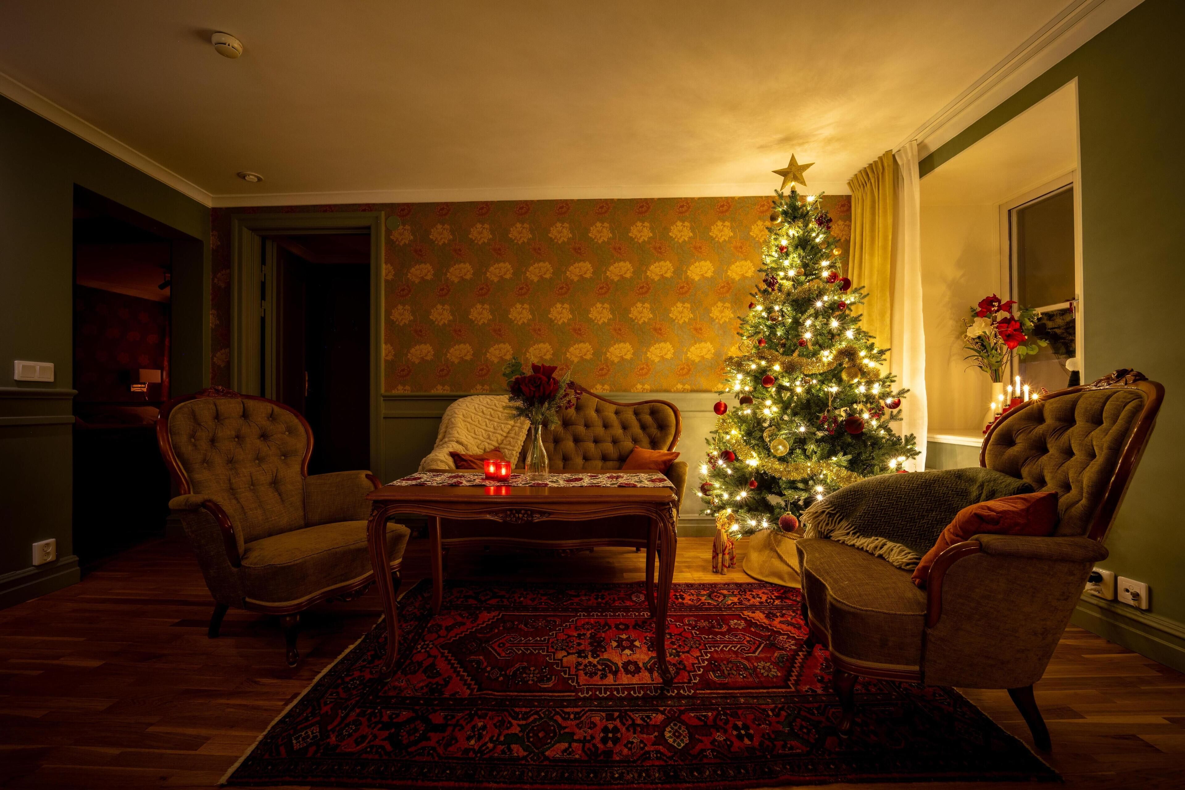 Una sala de estar acogedora con un árbol de Navidad, dos sillones, una mesa de centro y una alfombra estampada.