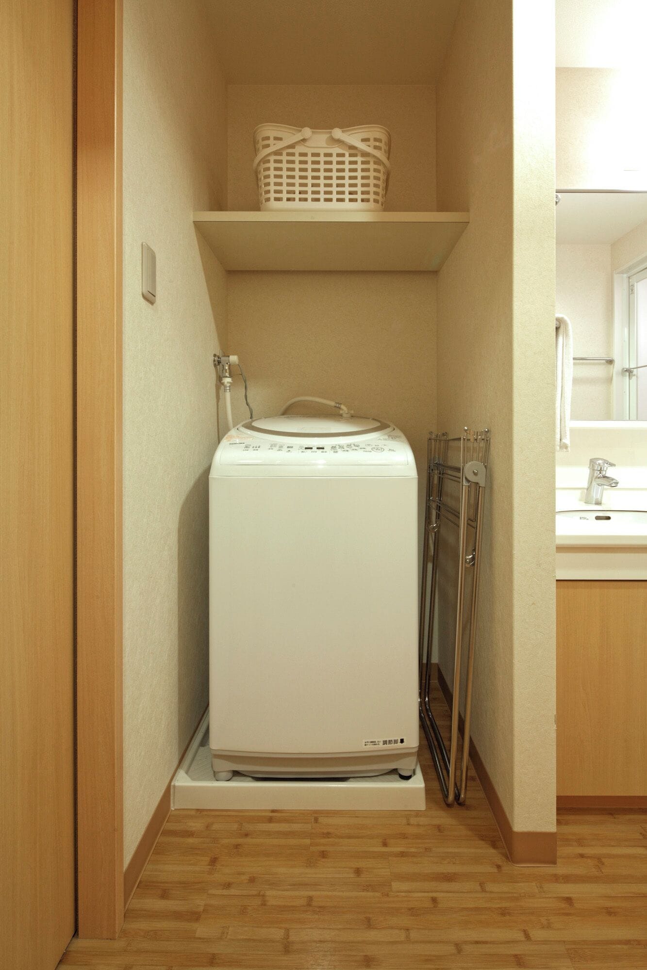 A compact laundry room with a washing machine, a drying rack, and a shelf with baskets.