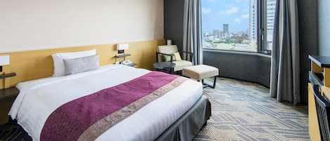 A hotel room with a large bed, a chair, a small table, and a view of the city.