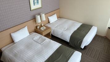 Habitación de hotel con dos camas, cada una con ropa de cama blanca y una manta verde. Entre las camas, hay una mesita de noche con un teléfono y un reloj.