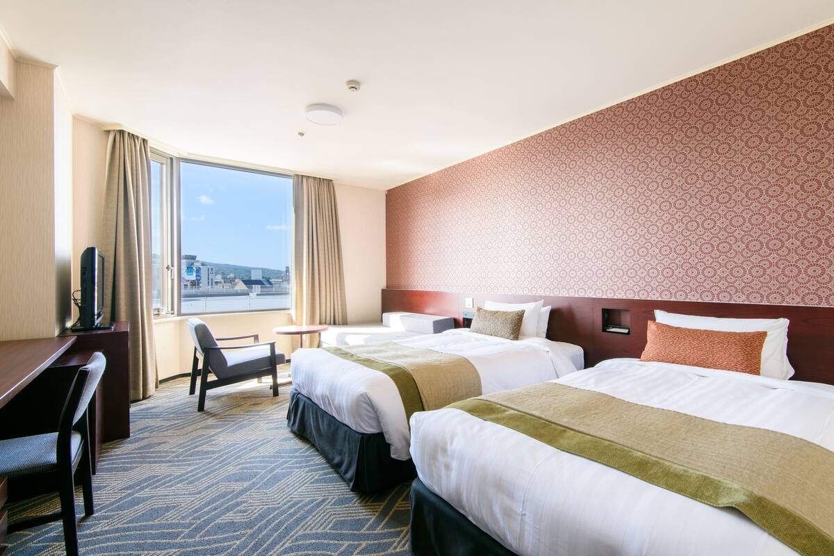 Hotellihuone, jossa on kaksi sänkyä, työpöytä ja tuoli.