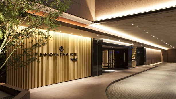 The exterior of the Kanazawa Hotel with a modern facade, a well-lit entrance, and a tiled pathway leading to the entrance.
