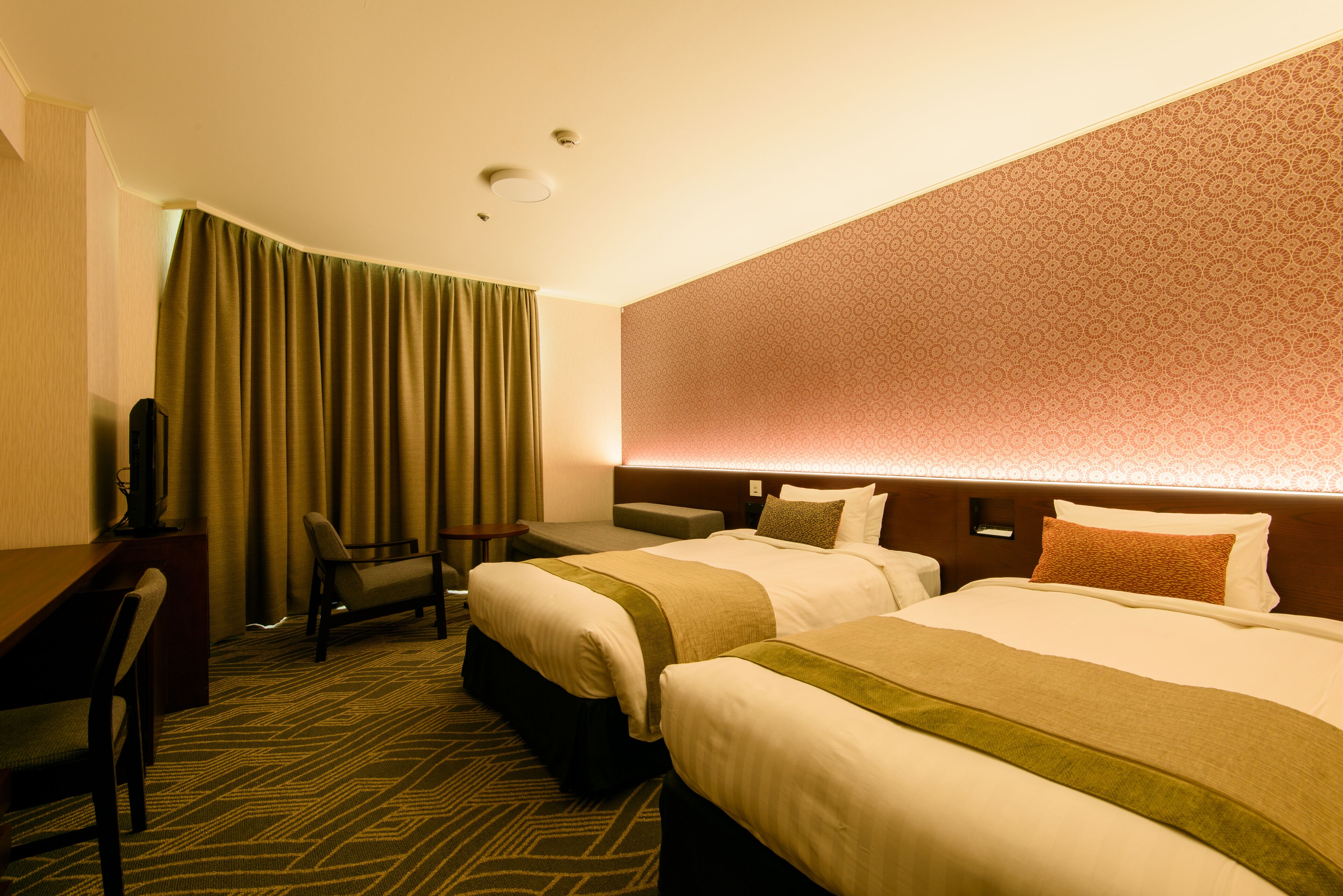A hotel room with two beds, a desk, a chair, and a large window with curtains.