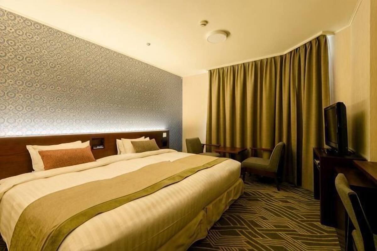 Hotellihuone, jossa on suuri sänky, työpöytä, tuoli, televisio ja kuviollinen seinä.