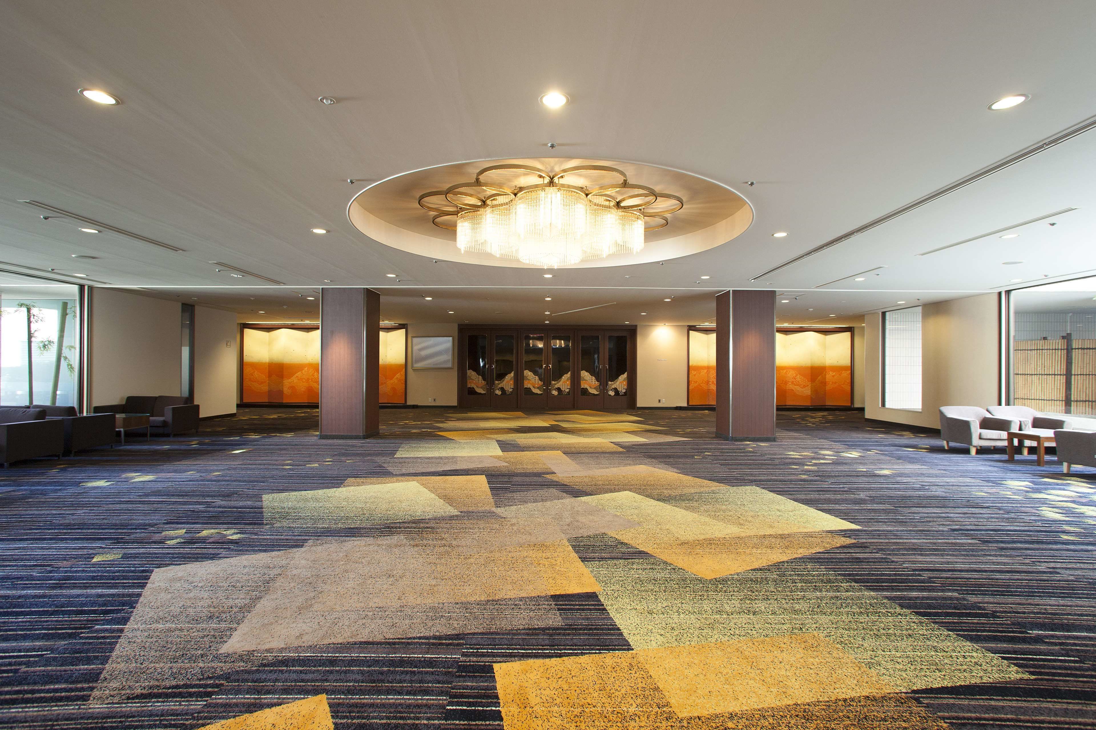 Un hall espacioso con alfombra estampada, un gran candelabro y zonas de estar.